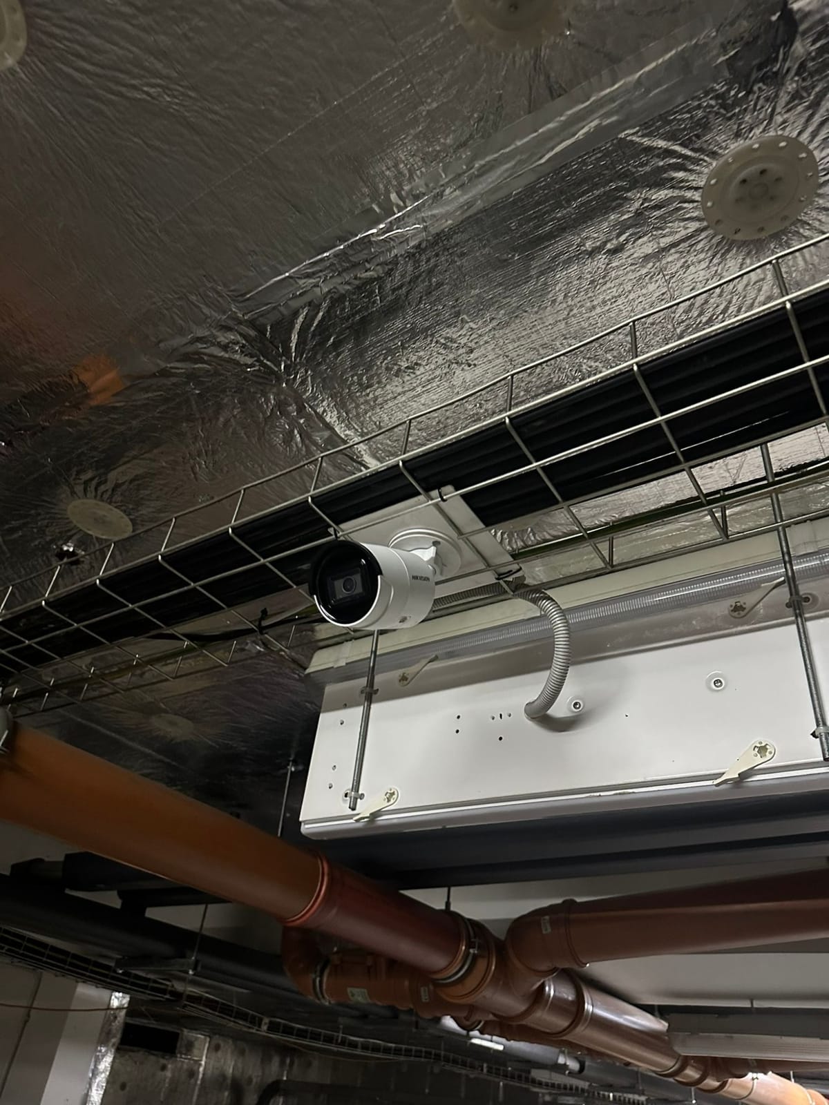 IP kamera Hikvision na bílém plastovém držáku v drátěném kabelovém žlabu pod stropem garáží