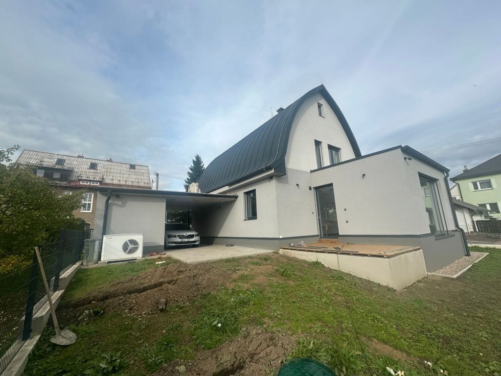 Dokončený dům: venkovní jednotka tepelného čerpadla a kryté stání s wallboxem