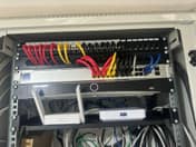 Datový rack: kabely barevně podle účelu (kamery, WiFi, data), switch UniFi a záznamník Hikvision
